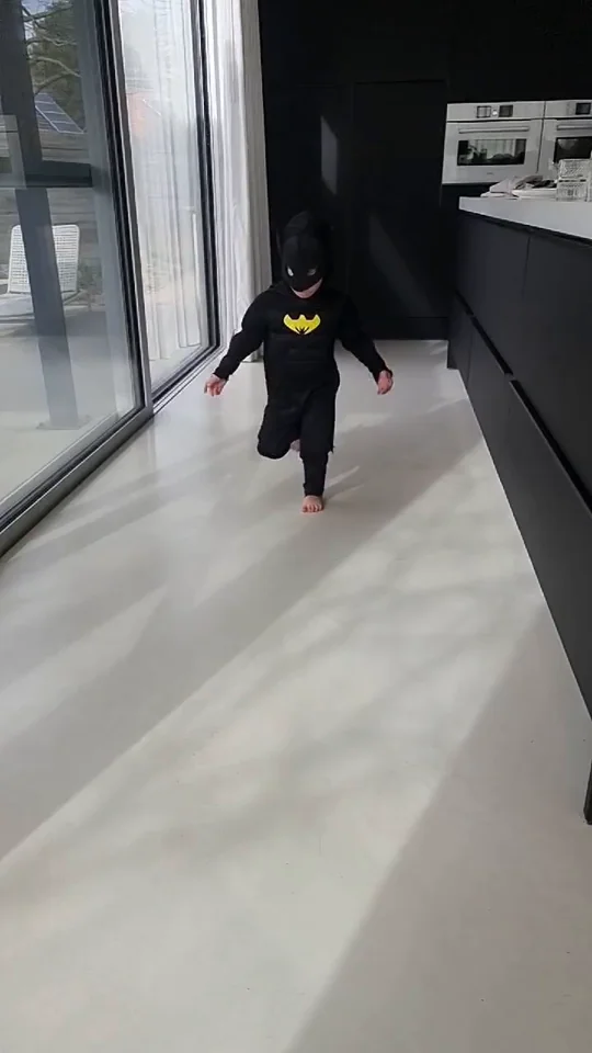 Kleine Batman op blote voeten op de gepolierde betonvloer in Lummen