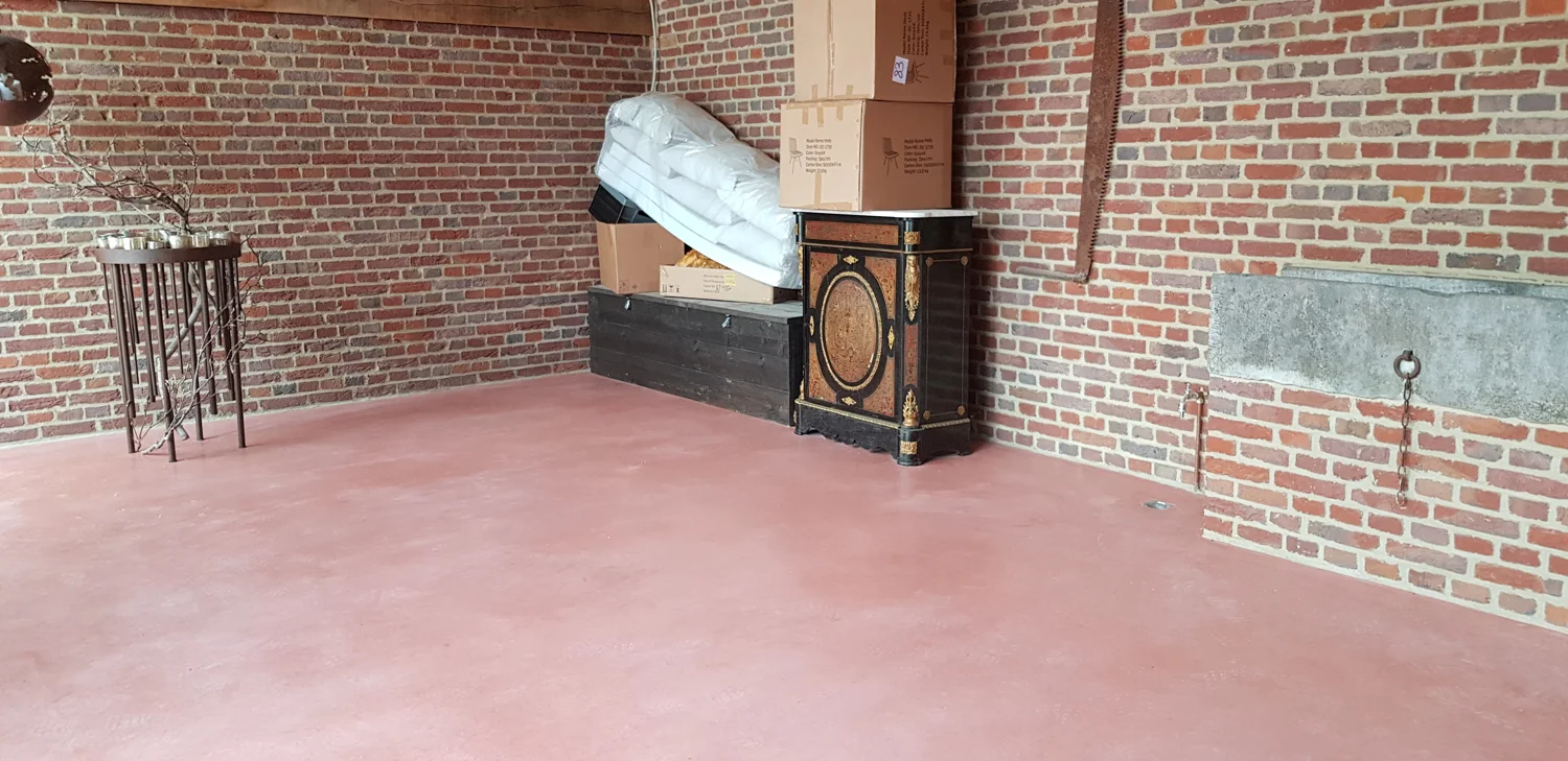 Terracottakleurige betonvloer tussen bakstenen muren in een hoeve in Kermt