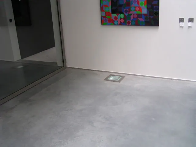 Cementkleurige woningvloer met kleurrijk kunstwerk aan de wand
