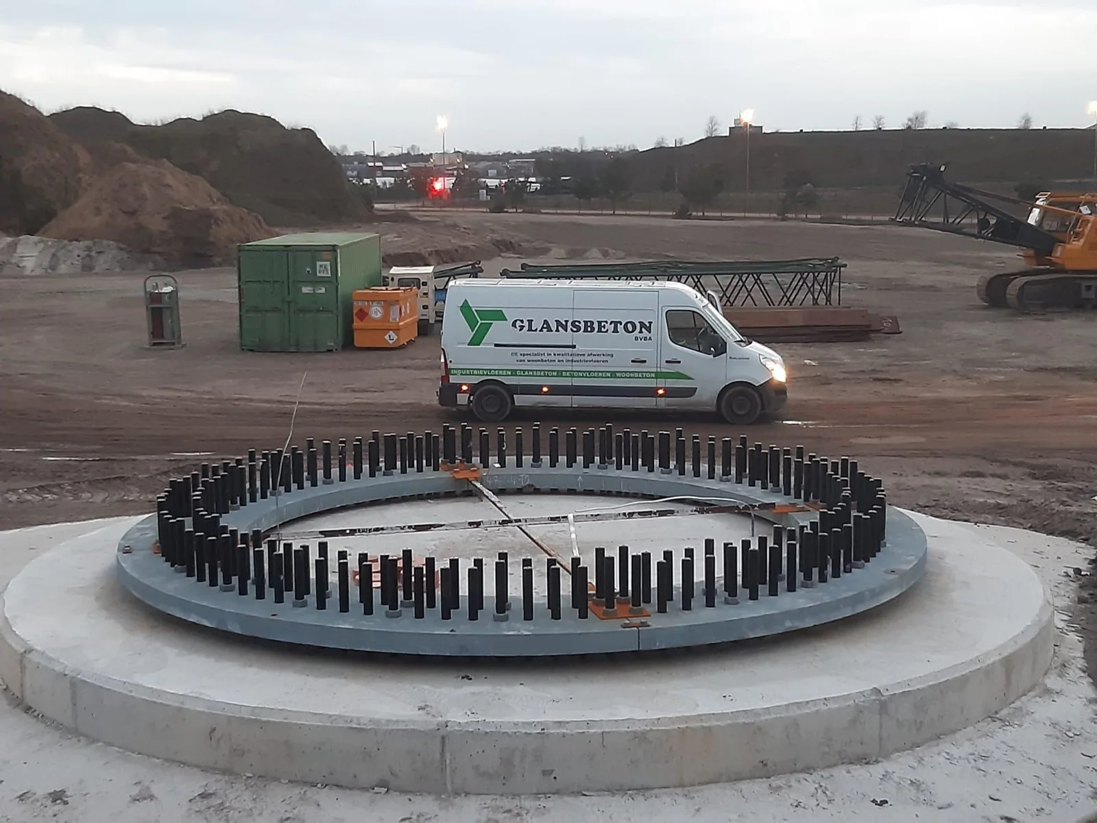 Ronde windturbinefundering met ankerbouten en een Glansbeton-bestelwagen op de werf