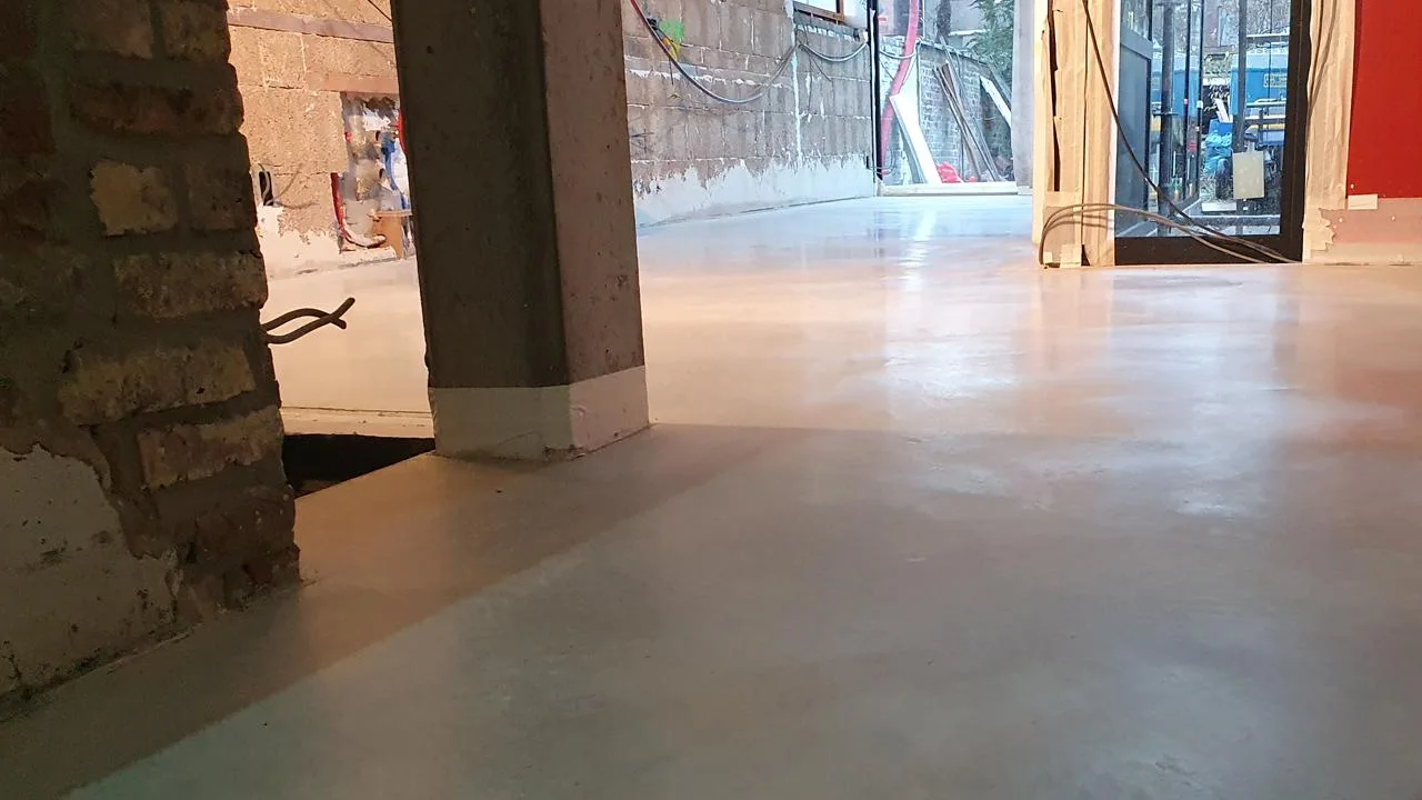 Gepolierde lichte betonvloer die doorloopt tussen twee ruimtes