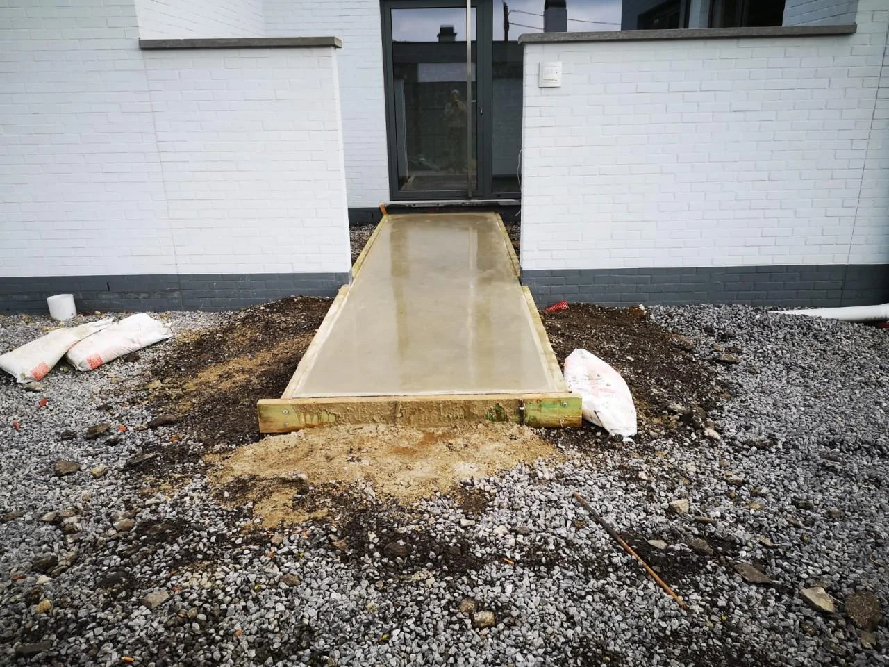 Zandkleurig betonpad naar de voordeur tussen witte gevels